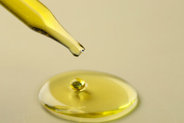 Cosmetic oil dripping from pipette on dark beige background, closeup. Space for text