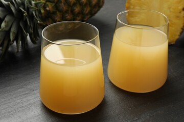 Tasty pineapple juice in glasses and fruits on grey textured table, closeup
