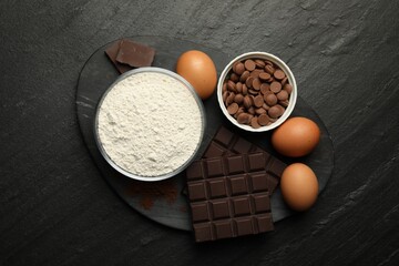 Flour, chocolate and eggs for making dough on dark textured table, top view