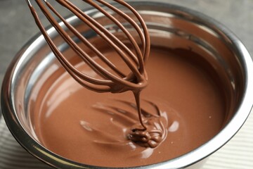 Chocolate dough dripping from whisk into bowl on table, closeup