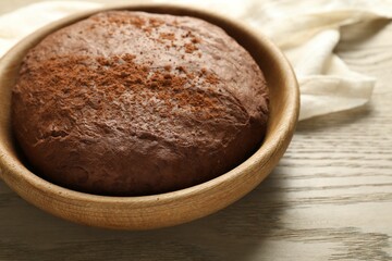 Chocolate dough in bowl on wooden table, closeup