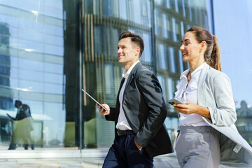 Two business professionals walk confidently outside a modern glass building, smiling in conversation.