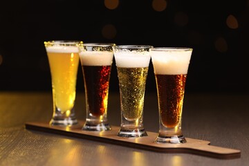Glasses with different types of beer on wooden table against black background, closeup