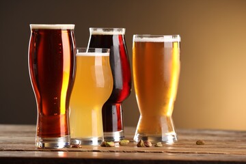Glasses with different types of beer and pistachio nuts on wooden table against color background, closeup