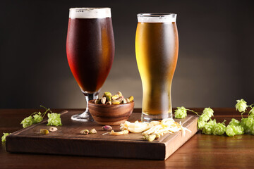 Glasses with different types of beer, snacks and fresh hops on wooden table
