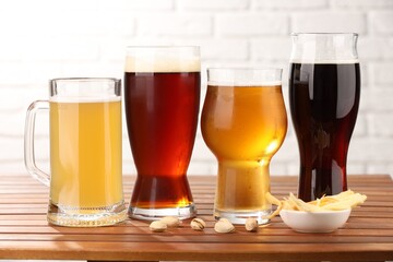Glasses with different types of beer and snacks on wooden table against white brick wall