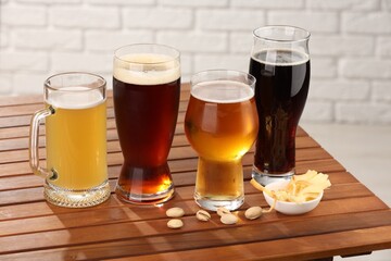 Glasses with different types of beer and snacks on wooden table against white brick wall