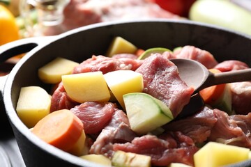 Cooking stew. Uncooked meat, vegetables and pot on black table, closeup