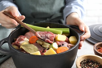 Woman preparing stew with vegetables and meat at white tiled table, closeup