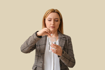 Upset adult woman suffering from headache with soluble tablet and glass of water on light background
