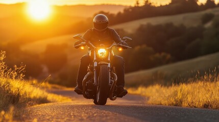 A motorcyclist rides along a winding road as the sun sets behind rolling hills, casting a golden glow on the landscape.