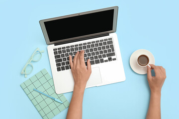 Female hands with laptop, notebook and cup of coffee on blue background