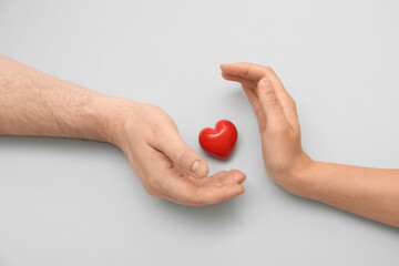 Hands of loving young couple with red heart on grey background