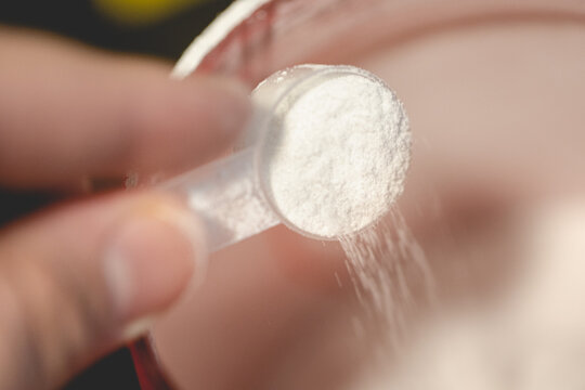Creatine. Close-up of a man holding a scoop of creatine and pouring it into a jar. Food supplement
