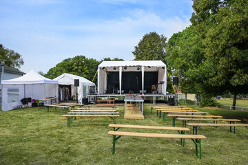 Open-air stage, tents for technical equipment and as dressing room, wooden benches for the audience, installed on a meadow for a music festival event in the countryside