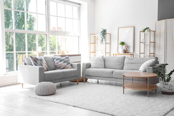 Interior of stylish modern living room with grey sofas and coffee table near big window