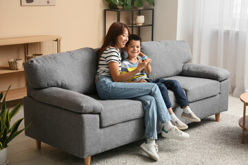Obraz premium Beautiful young happy Asian mother and cute little son plying with toy on sofa at home