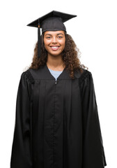 Young hispanic woman wearing graduation uniform with a happy face standing and smiling with a...