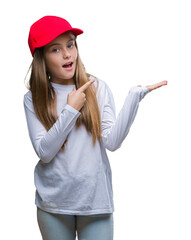 Young beautiful girl wearing red cap isolated background amazed and smiling to the camera while presenting with hand and pointing with finger.