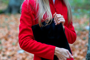 Autumn time. A girl on a walk in the forest in a red warm fleece jacket holds a work tablet in her...