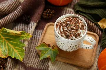 Autumn composition with cup of cocoa, leaves and wooden tray on plaid as background, closeup