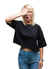 Fototapeta premium Young beautiful blonde woman over isolated background peeking in shock covering face and eyes with hand, looking through fingers with embarrassed expression.