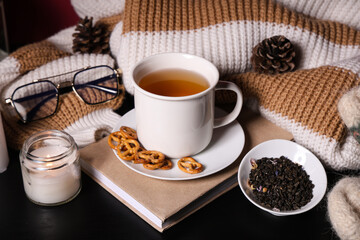Beautiful composition with book, cup of tea, winter decorations and warm clothes on black background