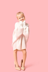 Cute little happy girl in warm stylish sweater and in oversized high heels on pink background