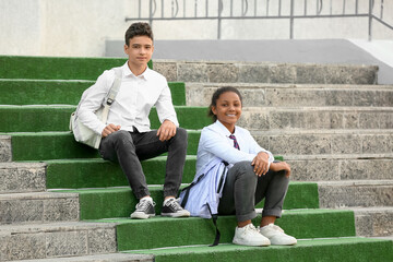 Group of happy pupils sitting on stairs near school outdoors