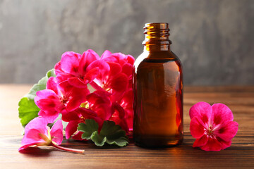 Geranium essential oil in bottle and beautiful flowers on wooden table