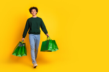 Full body portrait of nice young man store bags walk empty space wear sweater isolated on yellow...