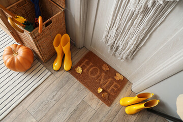 Doormat with autumn leaves and gumboots in hallway, top view