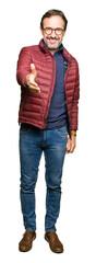 Obraz premium Middle age handsome man wearing glasses and winter coat smiling friendly offering handshake as greeting and welcoming. Successful business.