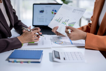 Businesswomen analyzing financial charts on paper and on a laptop screen, working together in the office