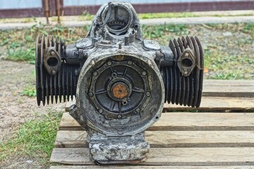 one rusty  heavy  iron  retro dirty mechanical  boxer  engine repaired from an old two-cylinder classic retro motorcycle stands on a wooden pallet during the day on the street	