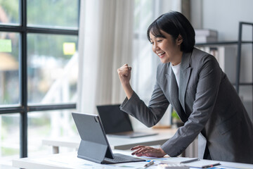 Excited businesswoman celebrating success looking at laptop in modern office