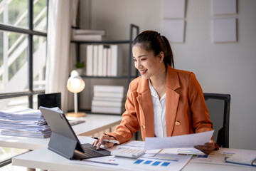 Asian accountant woman working with documents using calculator and laptop computer at office desk