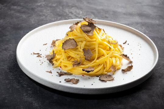 
Black truffle pasta Tajarin. Black rustic table, magical autumn light, front view. Autumn gourmet cuisine of Piedmont, Northern Italy, Spain and France