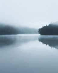 Fototapeta premium calm lake shrouded in morning fog, with faint silhouettes of trees in the distance