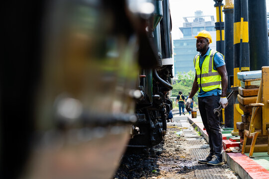 A man in a yellow vest stands next to a train. He is wearing a hard hat and is looking at the train
