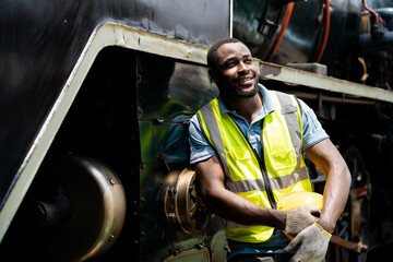 A man in a yellow vest stands next to a train engine. He is smiling and he is happy