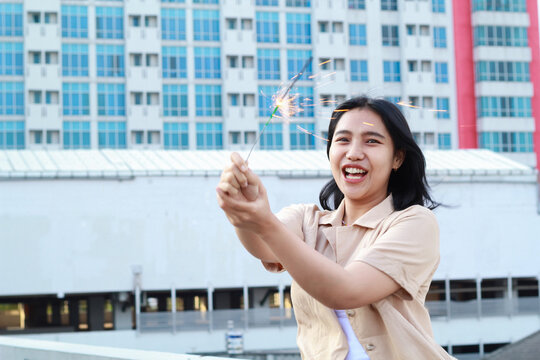 beautiful asian young woman holding sparklers firework and laughing in new year eve celebration standing in roof top outdoor with urban building background
