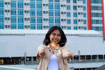 carefree asian young woman holding sparkler celebrate new year eve with laugh and dance in rooftop apartment outdoor with city building background