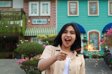 Fototapeta premium portrait of beautiful happy young asian woman holding sparklers fireworks to celebrate new year eve with garden party standing in outdoor vintage house yard