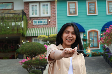Obraz premium happy young asian woman holding sparkler enjoy new year eve celebration in outdoor garden of colorful vintage house in evening