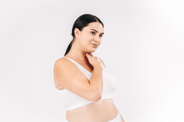 Fototapeta premium Full-figured young woman posing on a white studio background, exuding confidence and positivity. Perfect for promoting body positivity, fashion, and self-confidence, inspiring self-acceptance.