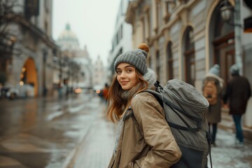 Obraz premium Young woman with a backpack strolls through a historic city street on a chilly day, enjoying the urban scenery and charm