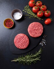 Fresh raw beef burgers for grilling with herbs and spices on black background