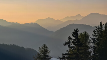 Serene mountain landscape at dawn in Gailtal Alps, Carinthia, Austria, Europe. Pine trees frame scene against morning sky. Distant peak Dobratsch in soft haze creating peaceful and serene atmosphere