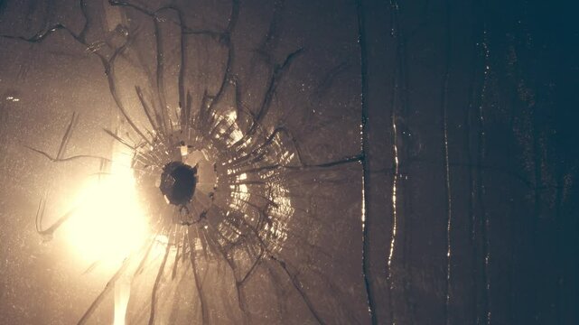 Bullet hole is in double pane of glass. Web of cracks, old web of spider debris is stirring in wind. Sweat streaks. Reflection of harsh sun in window. Concept of troubled world, war enters every home